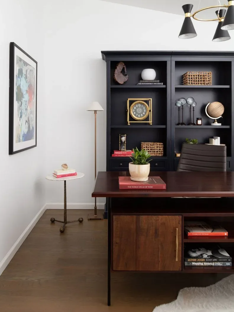 Wooden office desk with black shelving and a black ceiling light joined by gold-toned metal details.