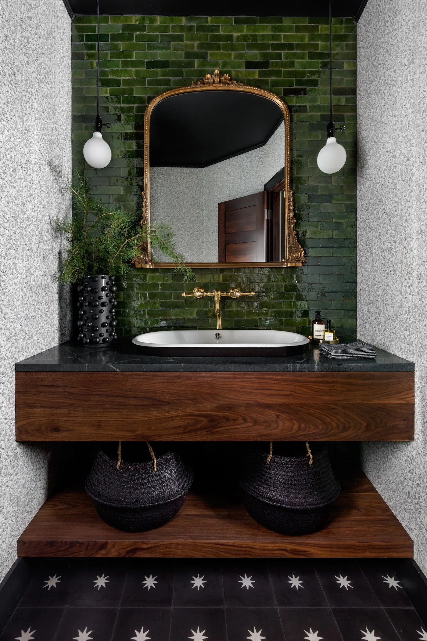 Compact wash area with green tiled wall, shaped warm-toned mirror and dark wood vanity