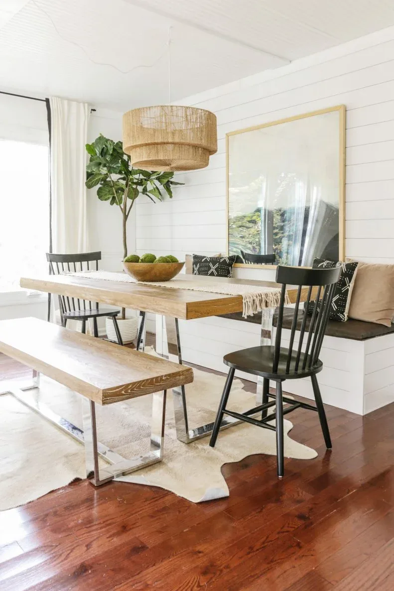 Wood dining table with black chairs, a wood bench and pale built-in seating against white paneling