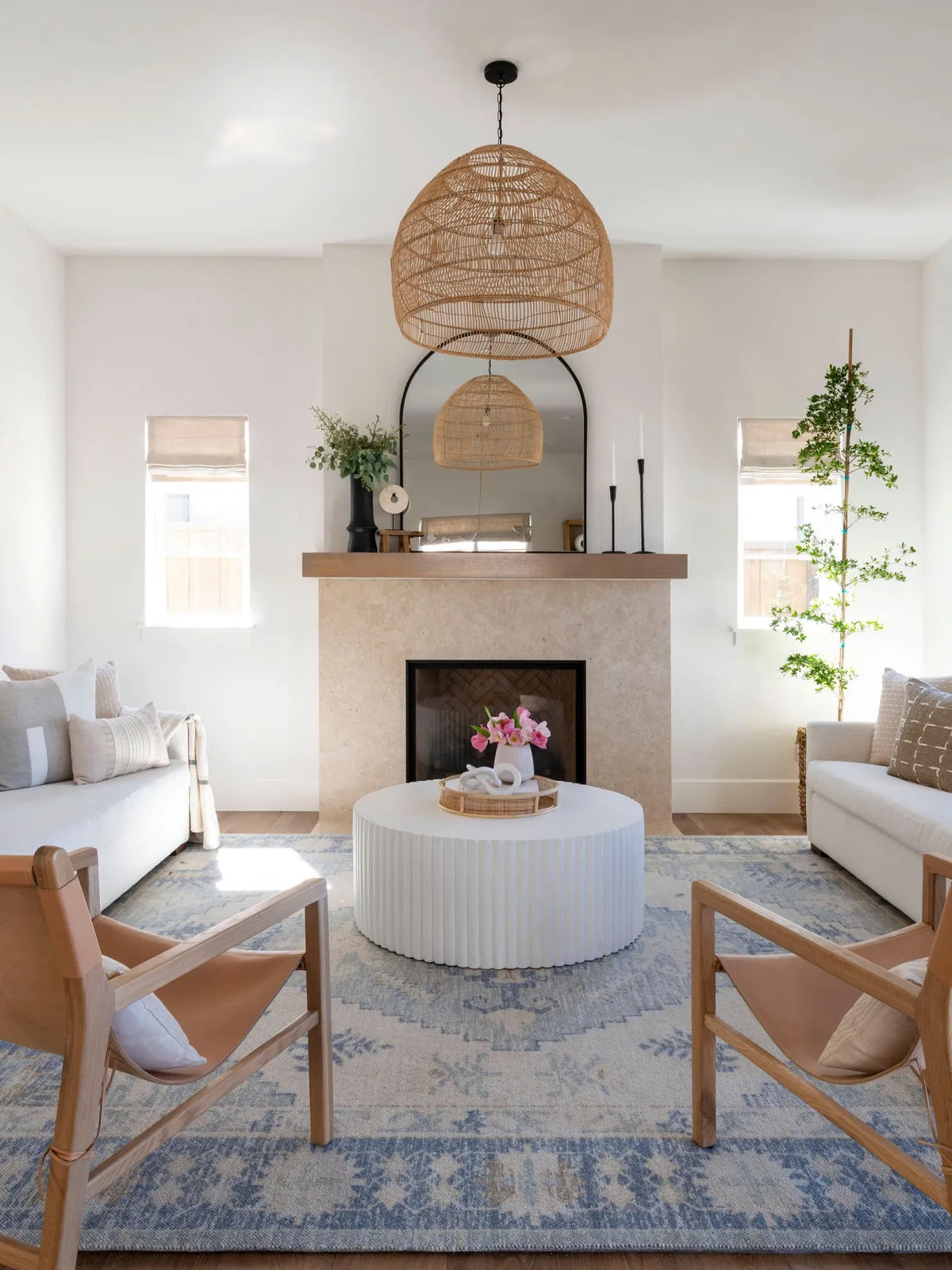Pale seating faces a quiet fireplace beside timber-framed chairs and a woven pendant.