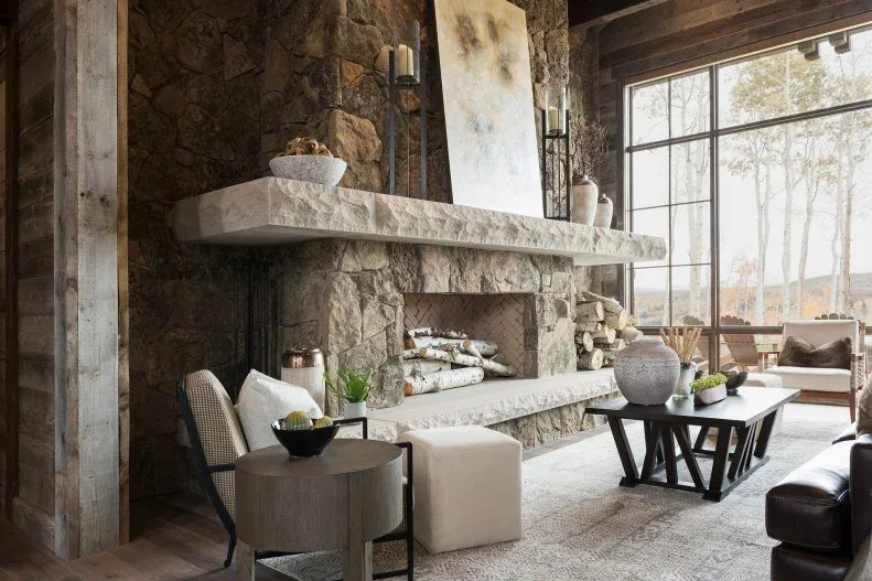 Large rough stone fireplace with thick projecting pale mantel, abstract picture, tall candles and dark timber beams nearby