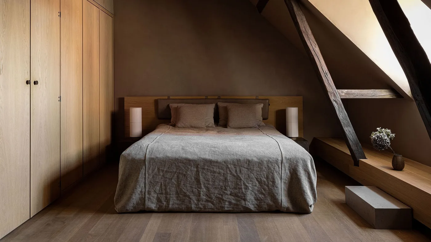 Brown-walled bedroom with full-height wood cupboards, pale gray bedding and a dark angled ceiling beam