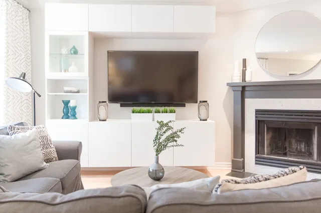 A television sits within pale storage beside a fireplace and light seating.