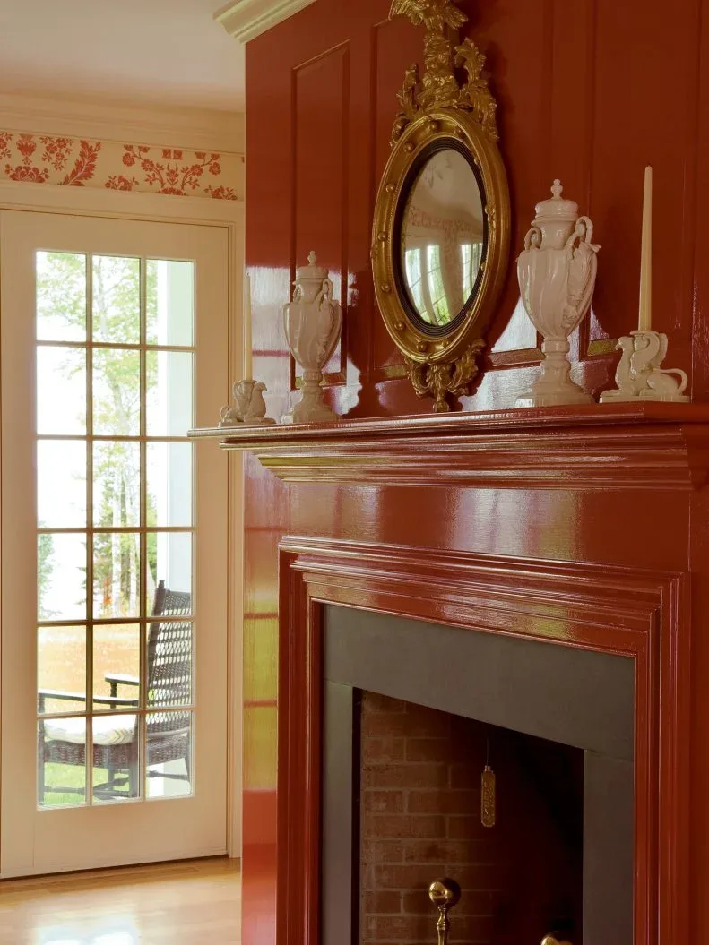 Glossy warm red paneled fireplace wall with ornate oval mirror and pale decorative vessels