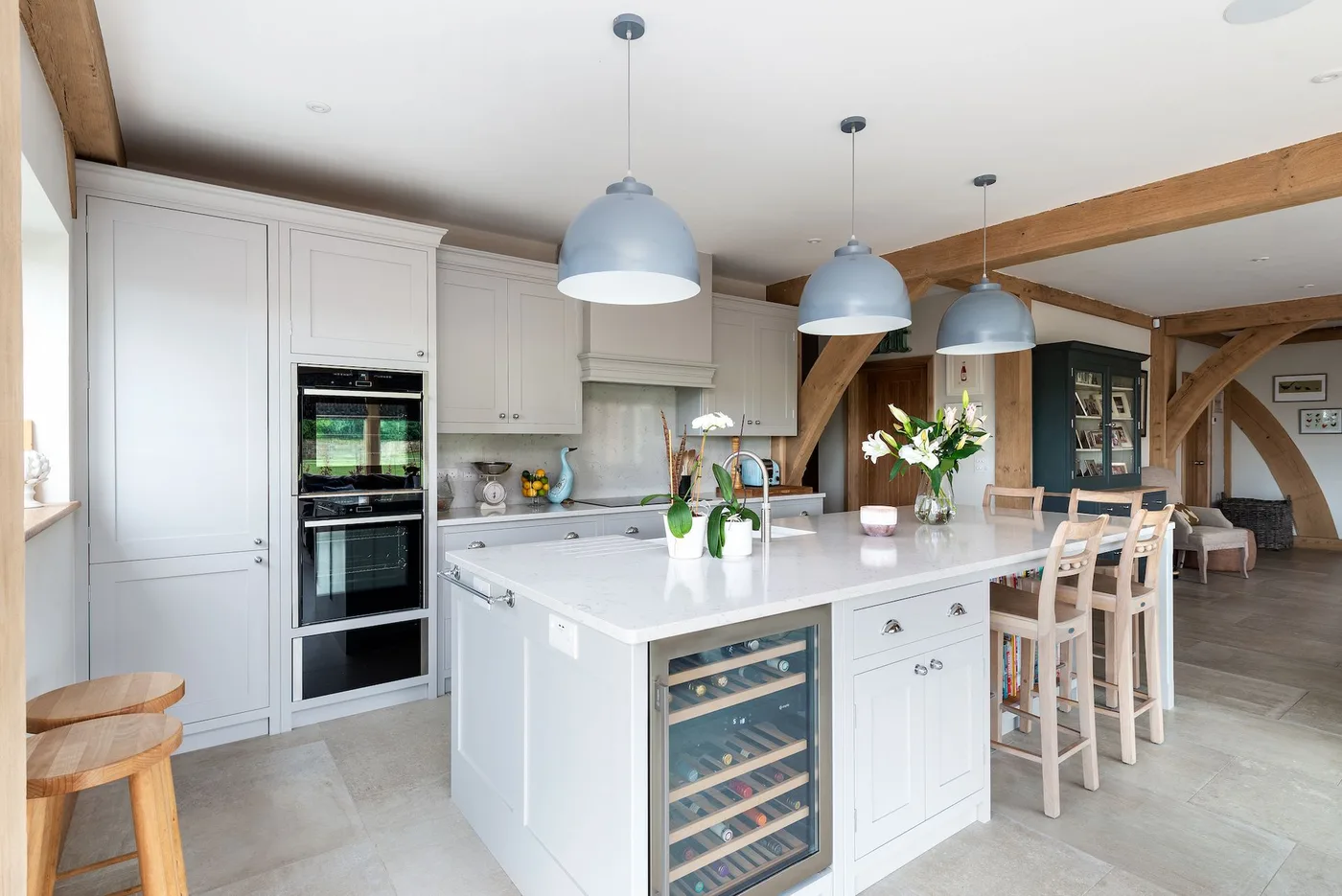 Cottage kitchen with white framed cabinets and island, exposed wooden beams, three pale blue hanging lights and stools along the island.