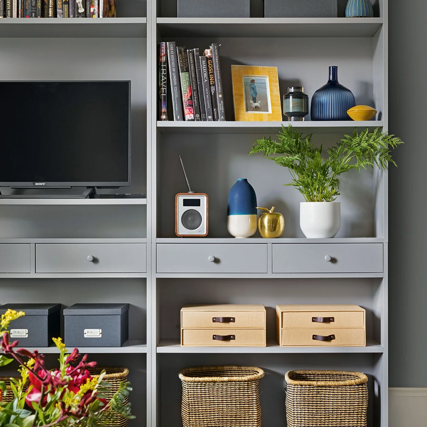 Gray built-in shelves surround a television and display books, blue vases, drawers and baskets