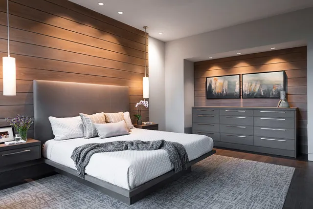 A dark upholstered bed sits against horizontal timber boards beside a wide drawer unit.