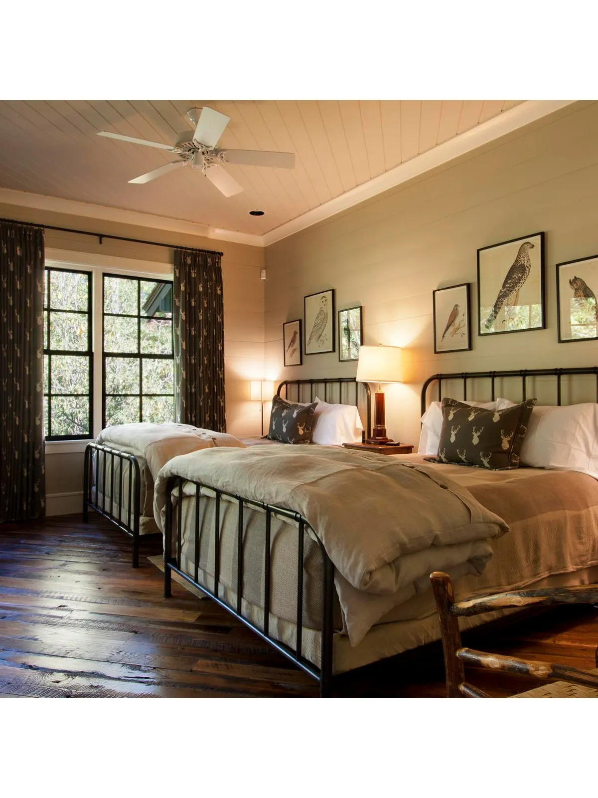 Two dark metal beds stand beside warm timber floors, framed bird pictures and shared bedside lighting.