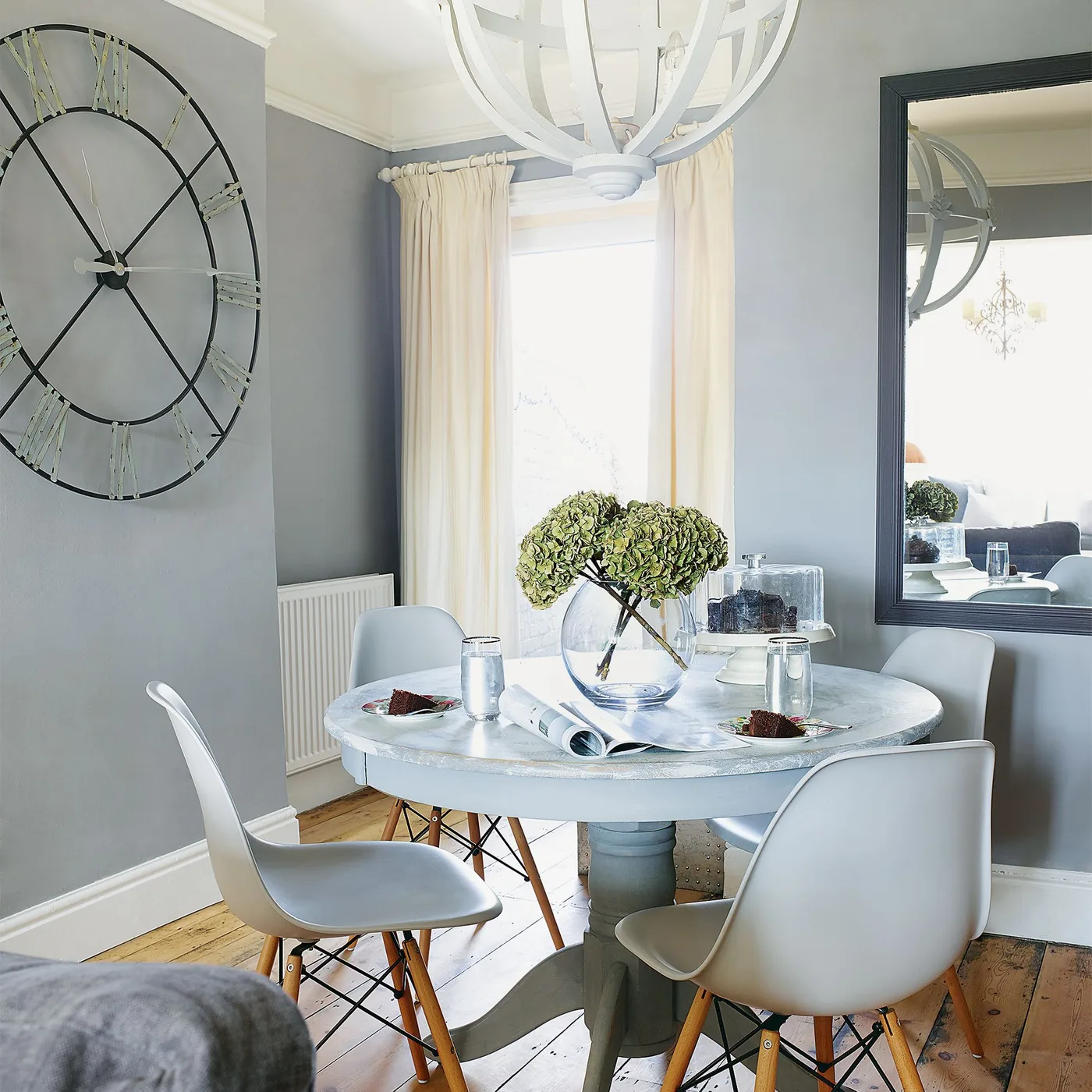 Dark-framed rectangular mirror beside a round pale dining table and an oversized open wall clock