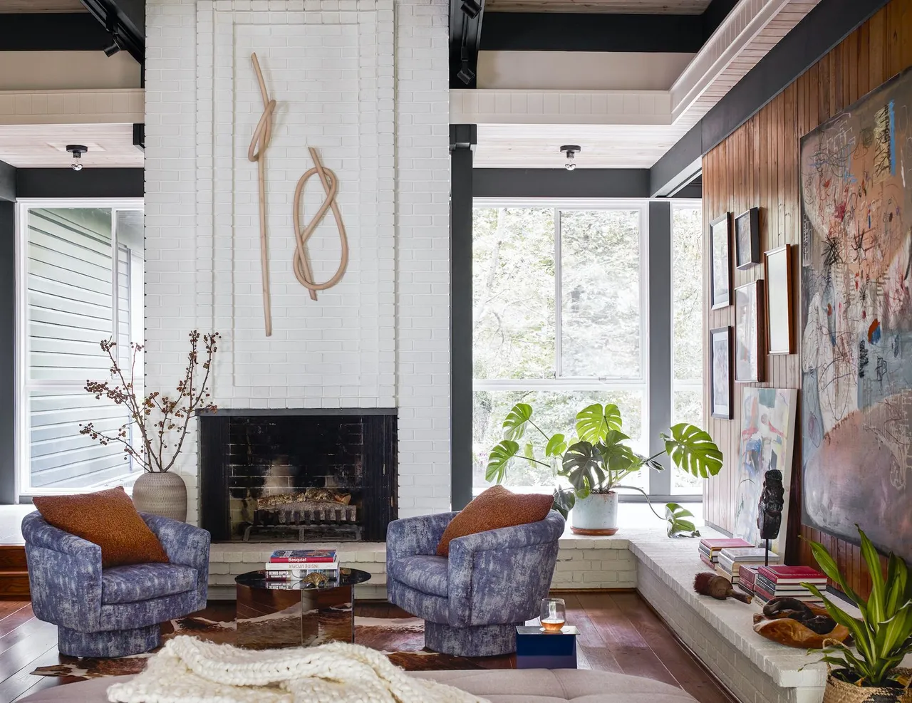 Two patterned chairs face a low table beside a tall pale fireplace and a timber wall.
