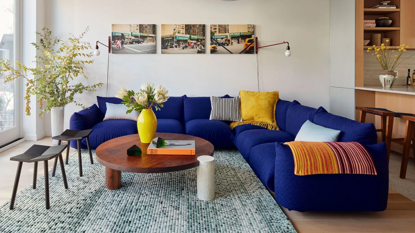 Blue sectional with pale striped pillows, a yellow pillow and a colorful striped throw.
