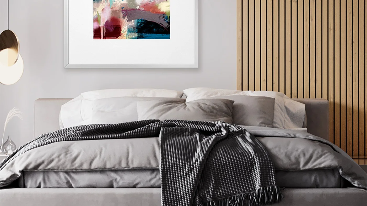 A bed with gray bedding sits beside a vertical wooden slat panel, pale walls, a colorful framed picture and a rounded wall light