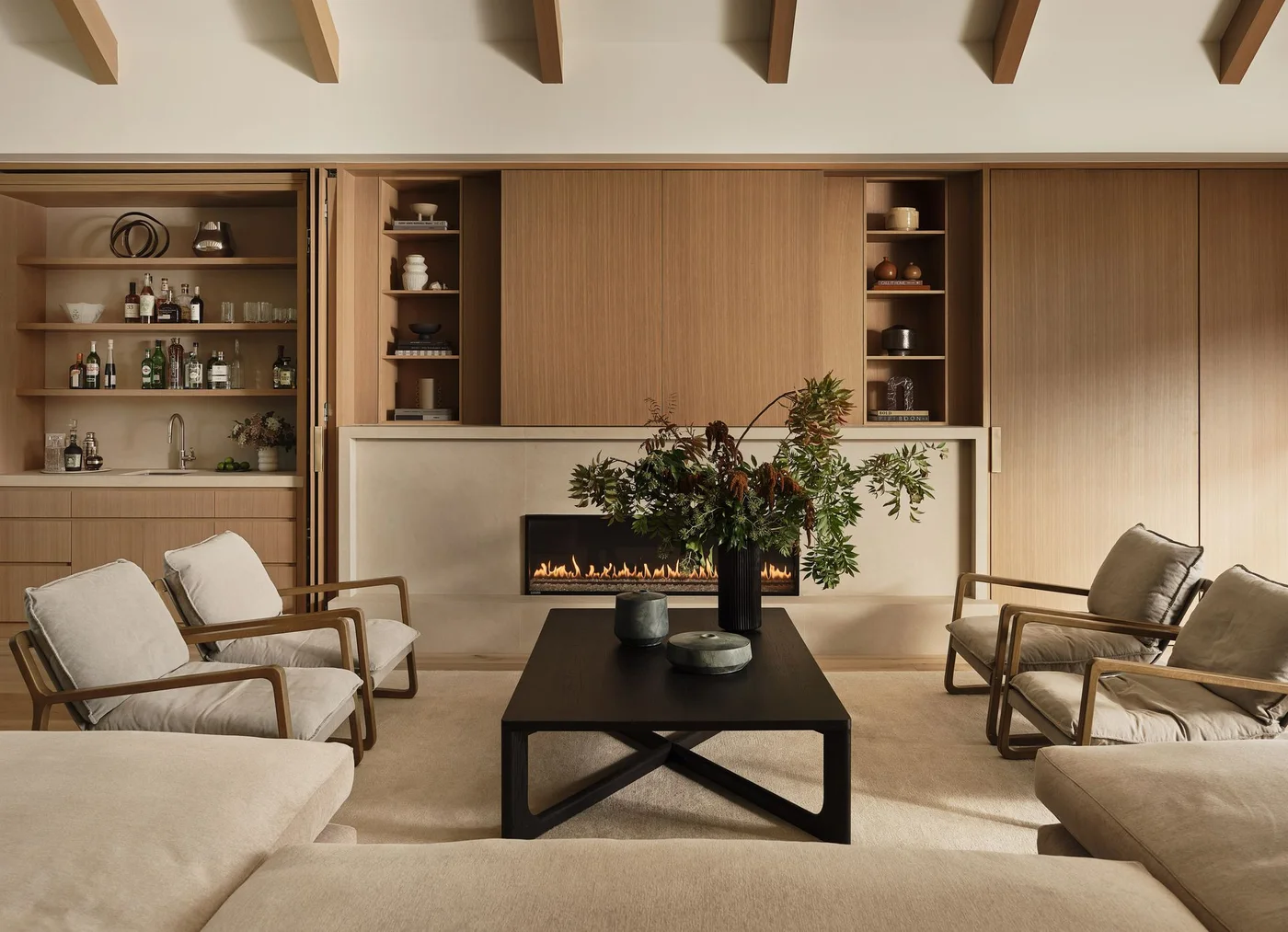 Wooden sliding panels and open shelves form a media wall above a pale fireplace behind light chairs and a dark table