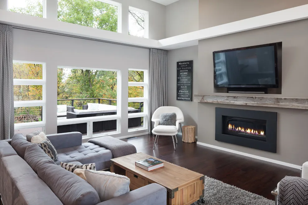A gray sectional faces a television and fireplace beneath a large window