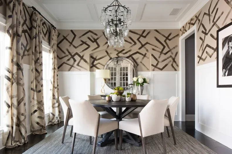 Dining room with tall white lower-wall panels, patterned upper walls, pale chairs and a round mirror