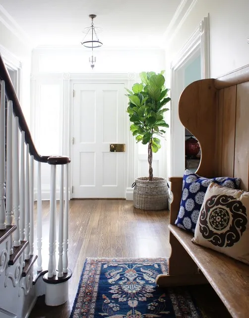 A dark timber bench with patterned cushions sits beside pale walls and a blue patterned runner.