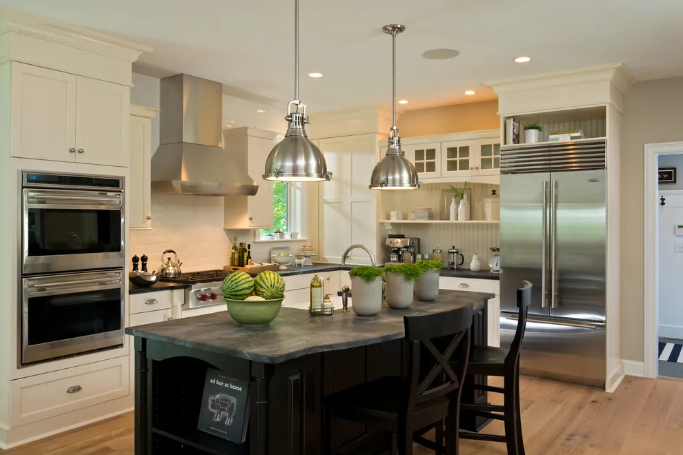 Warm white paneled cabinets surround a dark island beneath metal pendants