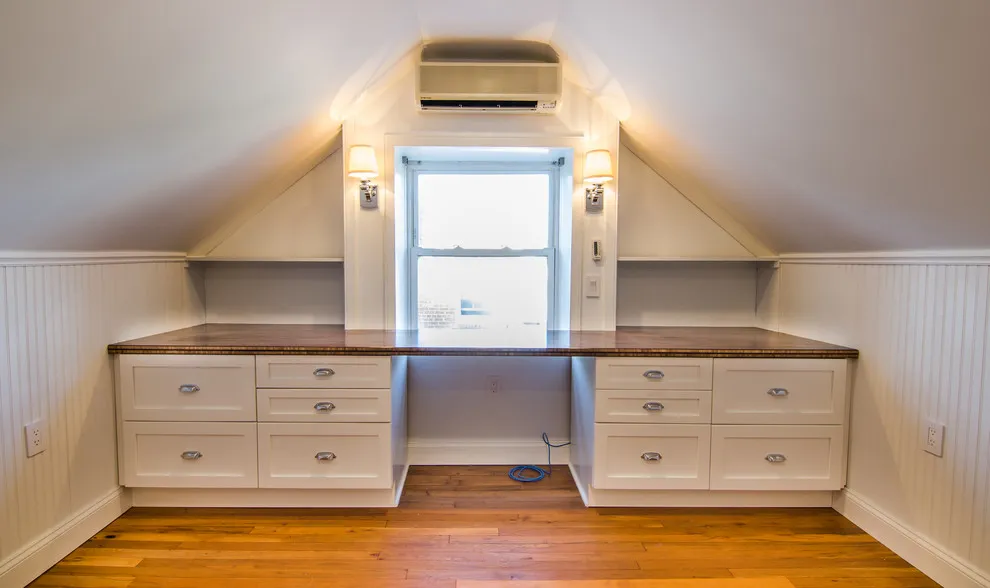 A dark timber desktop over cream drawers sits beneath an attic window