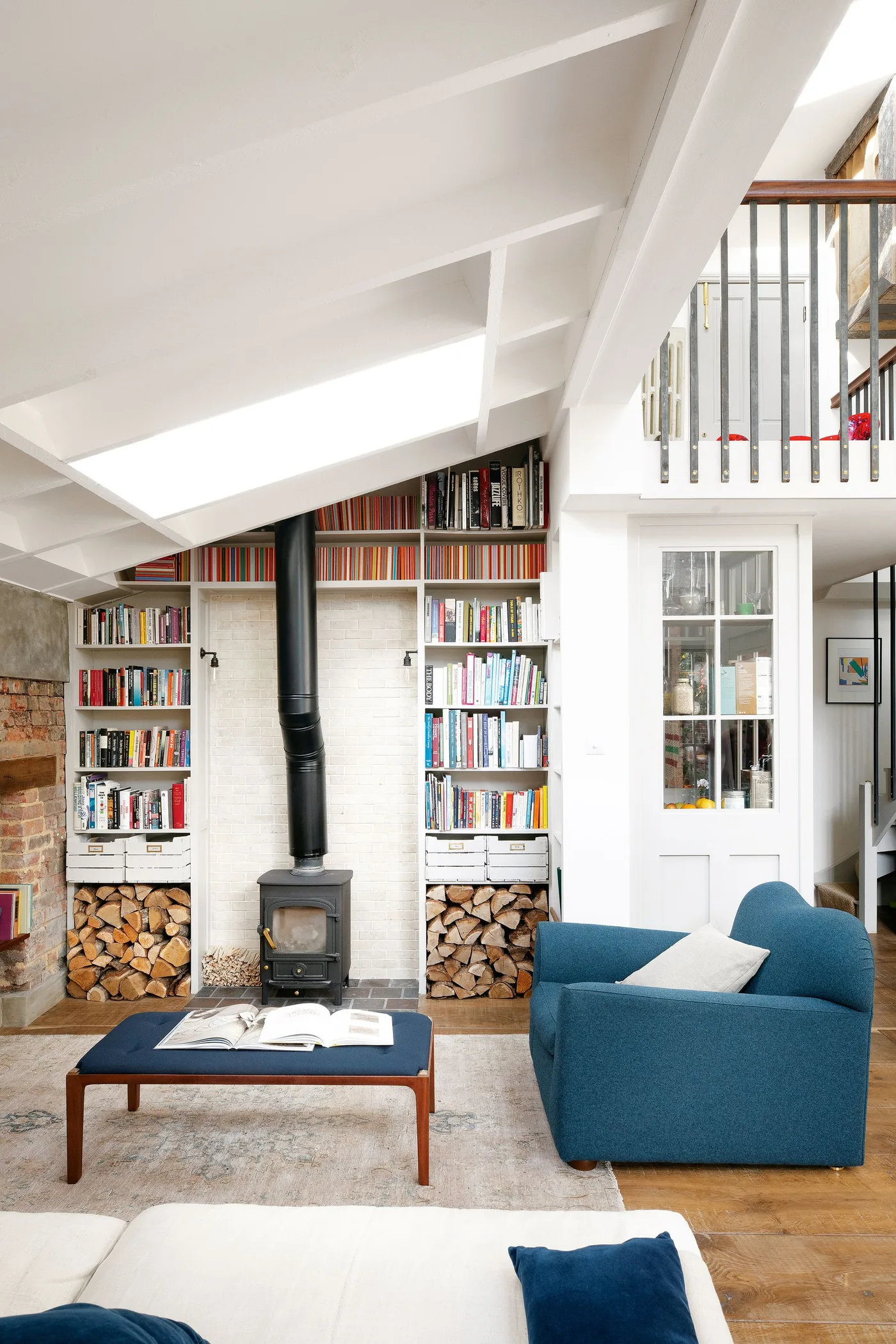 White bookcases and lower log compartments beside black stove under sloping ceiling