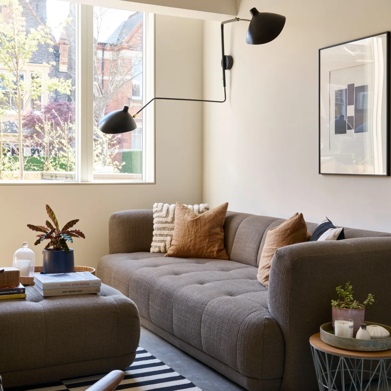 A dark sofa sits beside a window beneath adjustable wall lamps