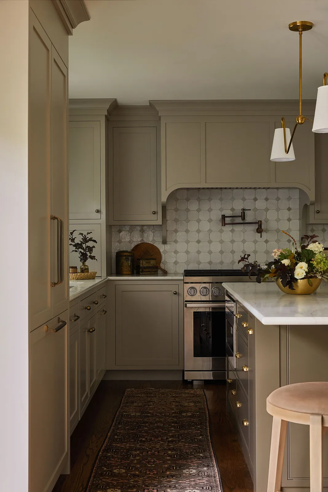 Muted beige-gray cabinets surround a narrow kitchen with a patterned runner