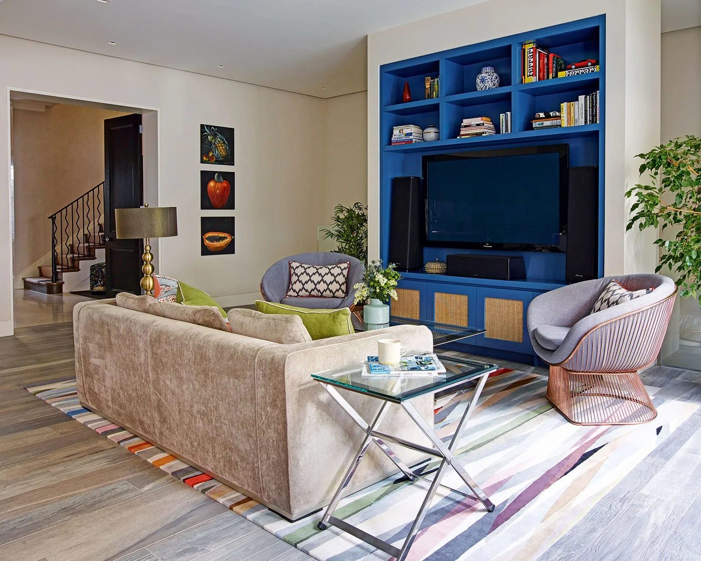 A television is framed by blue shelves and lower cabinets behind a beige sofa, pale chair and transparent side table