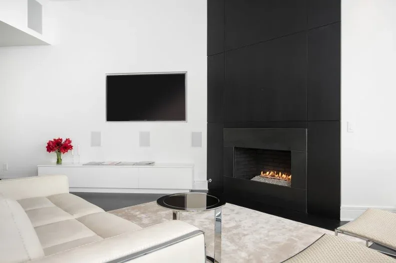 Tall black paneled fireplace face beside white wall with television, low white cabinet and pale seating