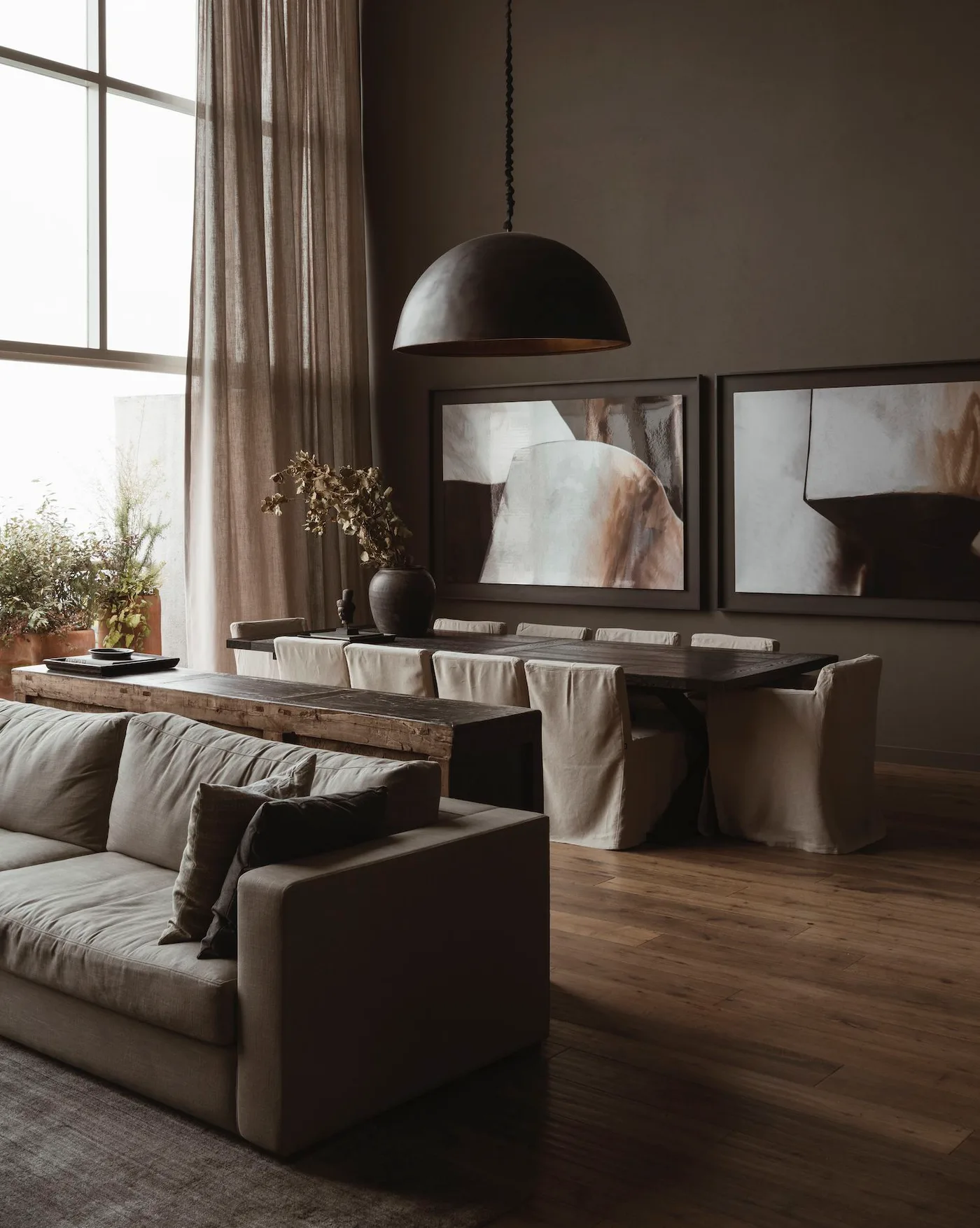 Brown living and dining room with pale sofa, wood console, upholstered dining chairs and large framed pictures