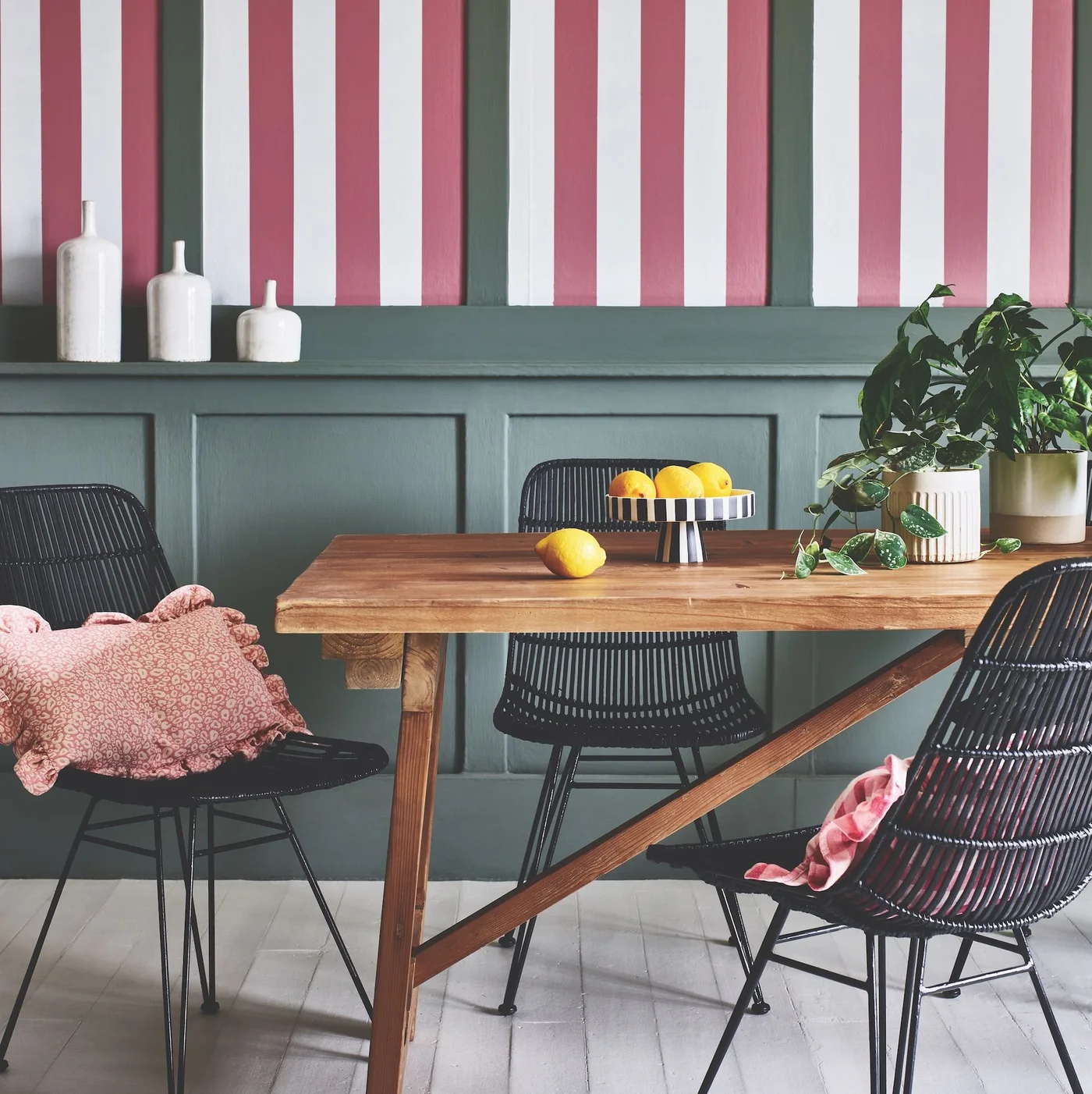 Green lower wall paneling sits beneath pale and red vertical stripes beside a wooden table with dark chairs and pink cushions