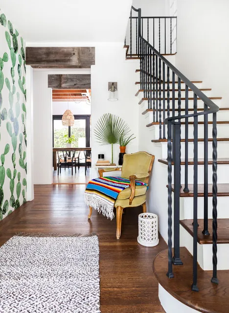 A vintage upholstered chair with a colorful striped throw sits beside a dark stair rail and leafy-patterned wall.