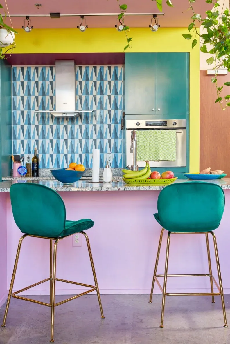 Teal kitchen cabinets, triangular blue backsplash tiles and a pink island with matching teal stools.
