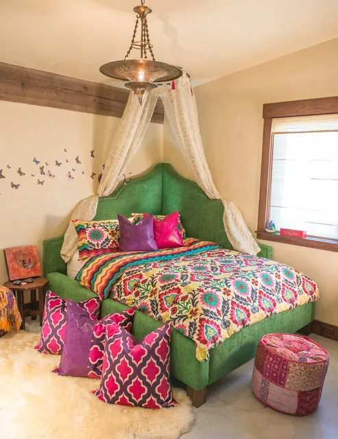 A richly patterned bedcover sits beneath a pale canopy in a timber-trimmed bedroom.