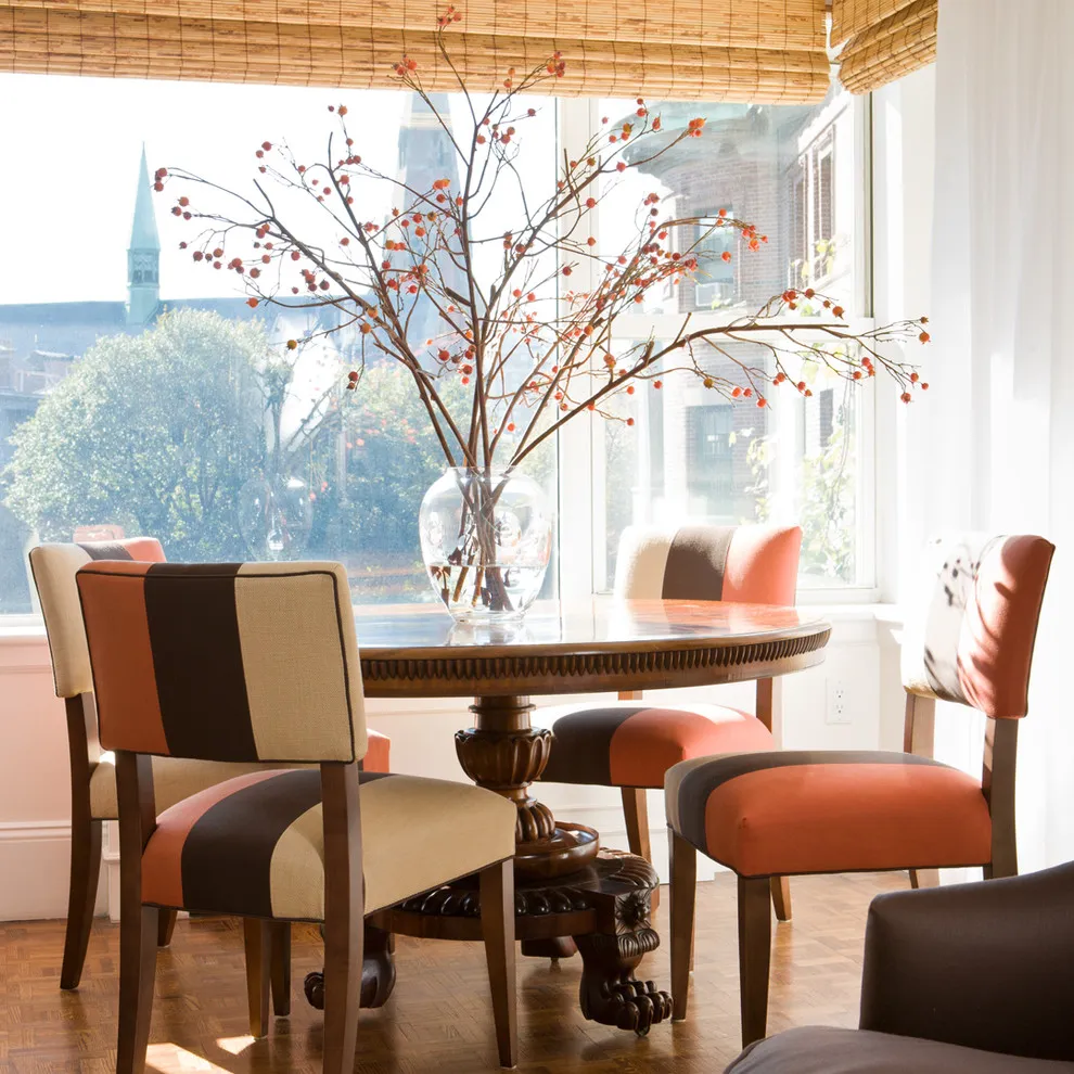 Upholstered dining chairs in warm neutral colors surround a round table beside tall windows