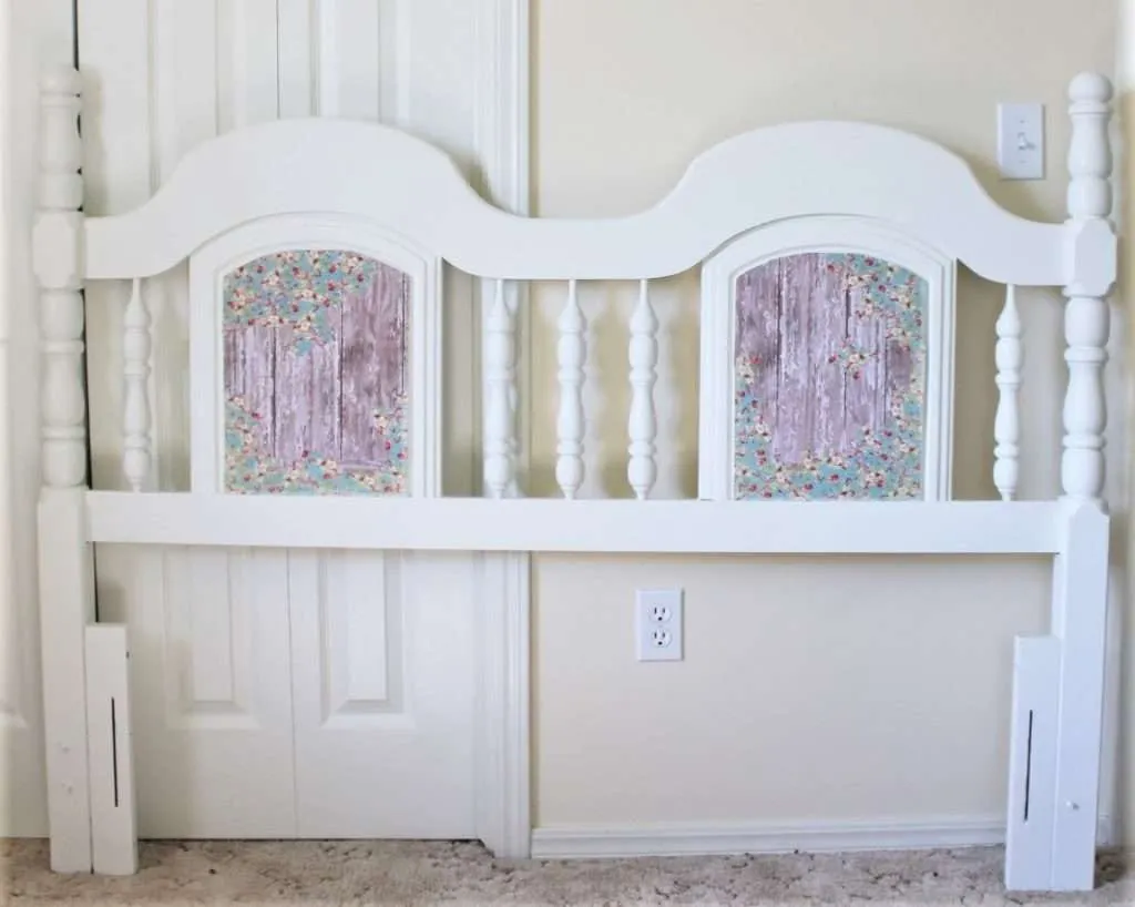 A pale spindle headboard includes small floral panels against a light wall.