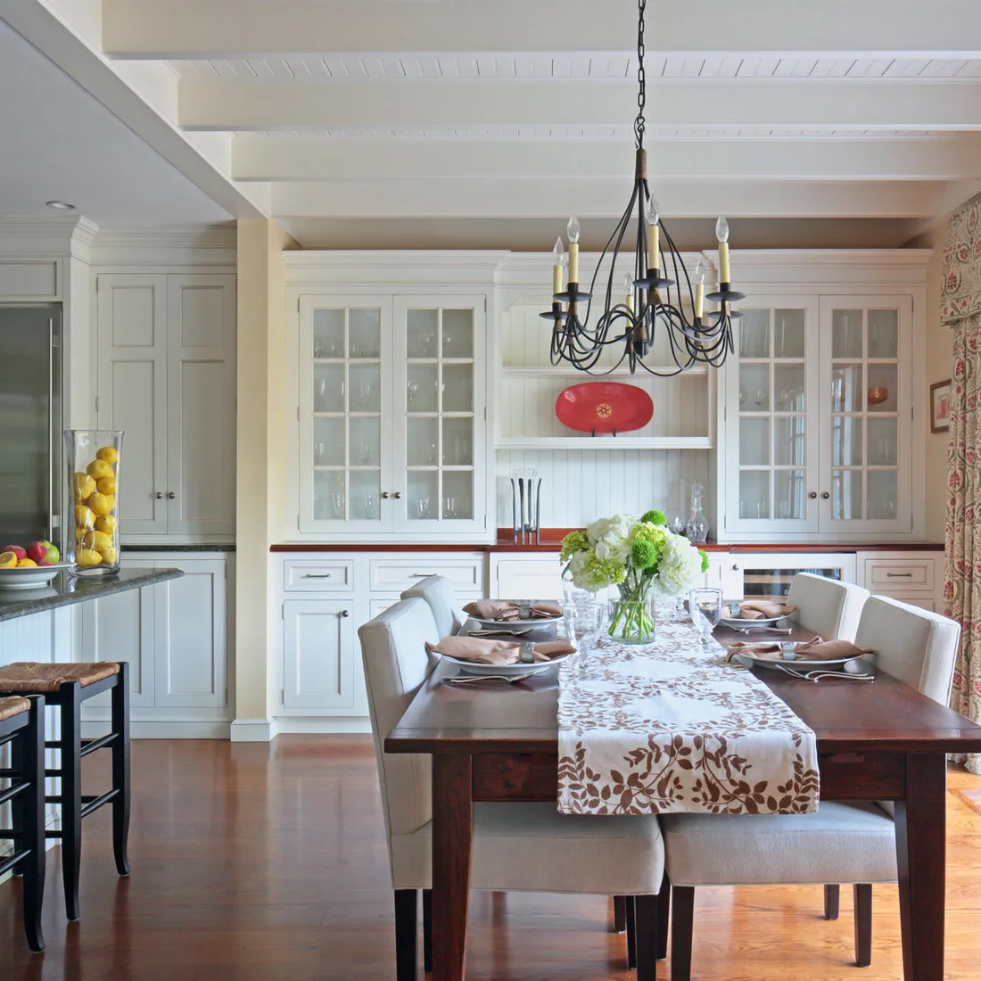 White dining hutch with glazed side cupboards and open central shelves behind a set wood table