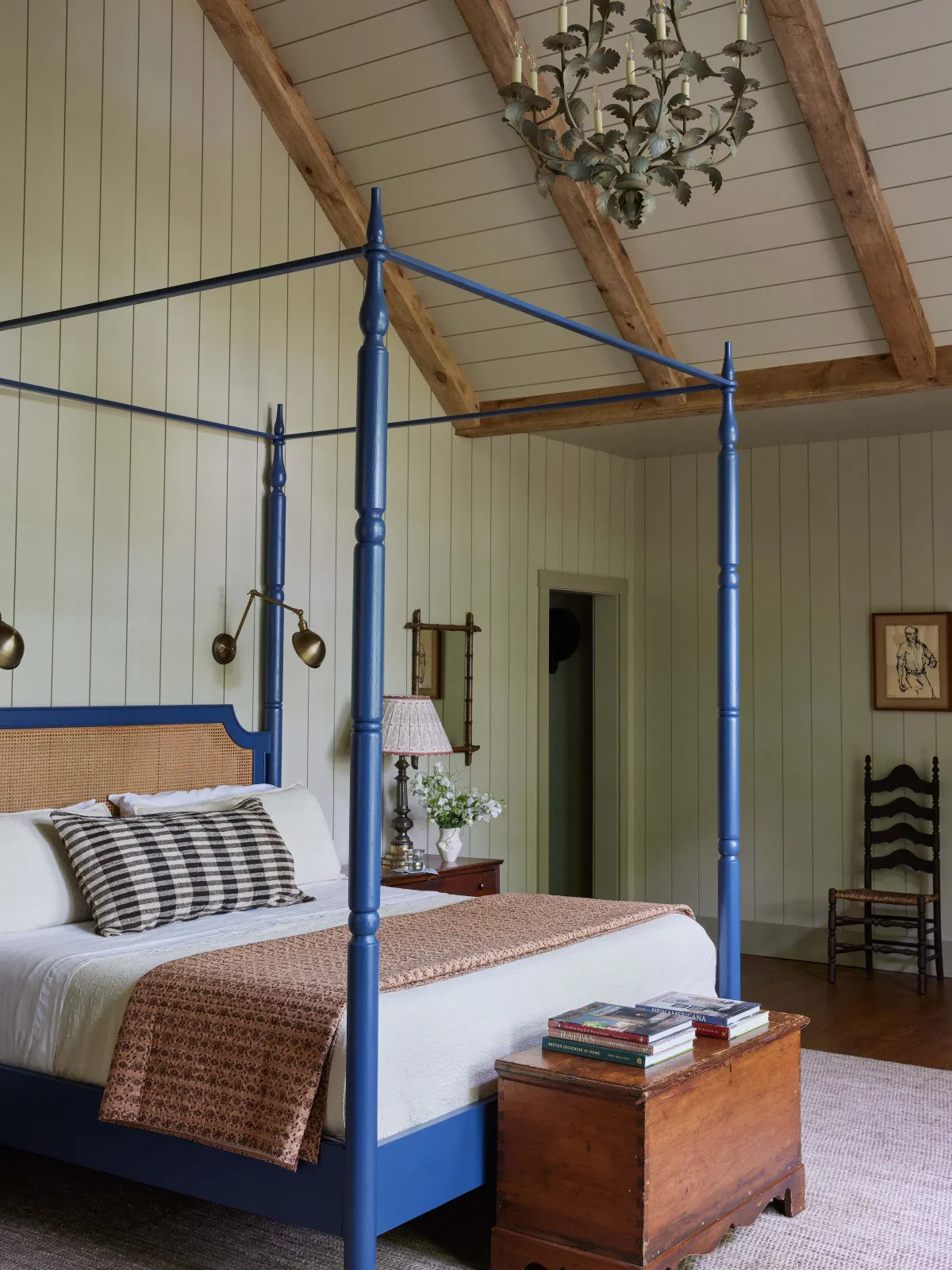A blue painted four-poster bed stands against pale vertical boards beneath timber beams.
