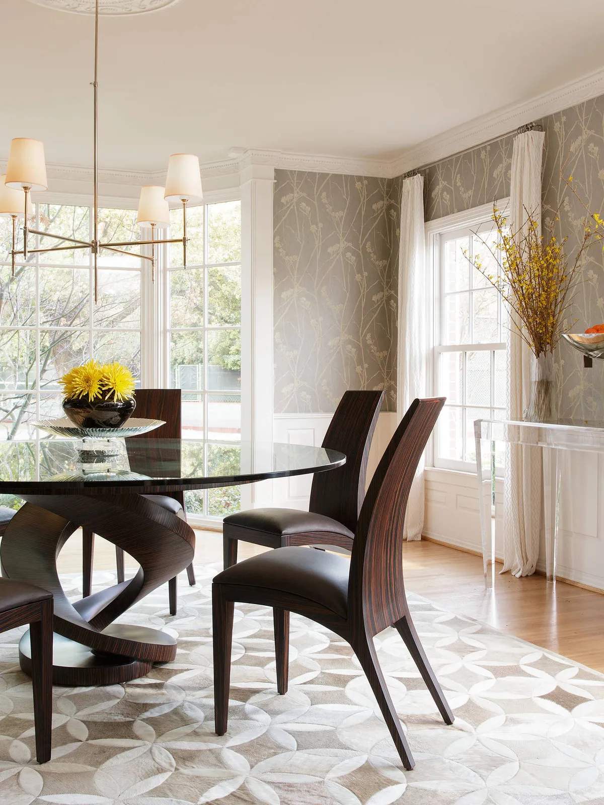 Subtle pale wall pattern surrounds a dark dining table and sculptural chairs beside light curtains.