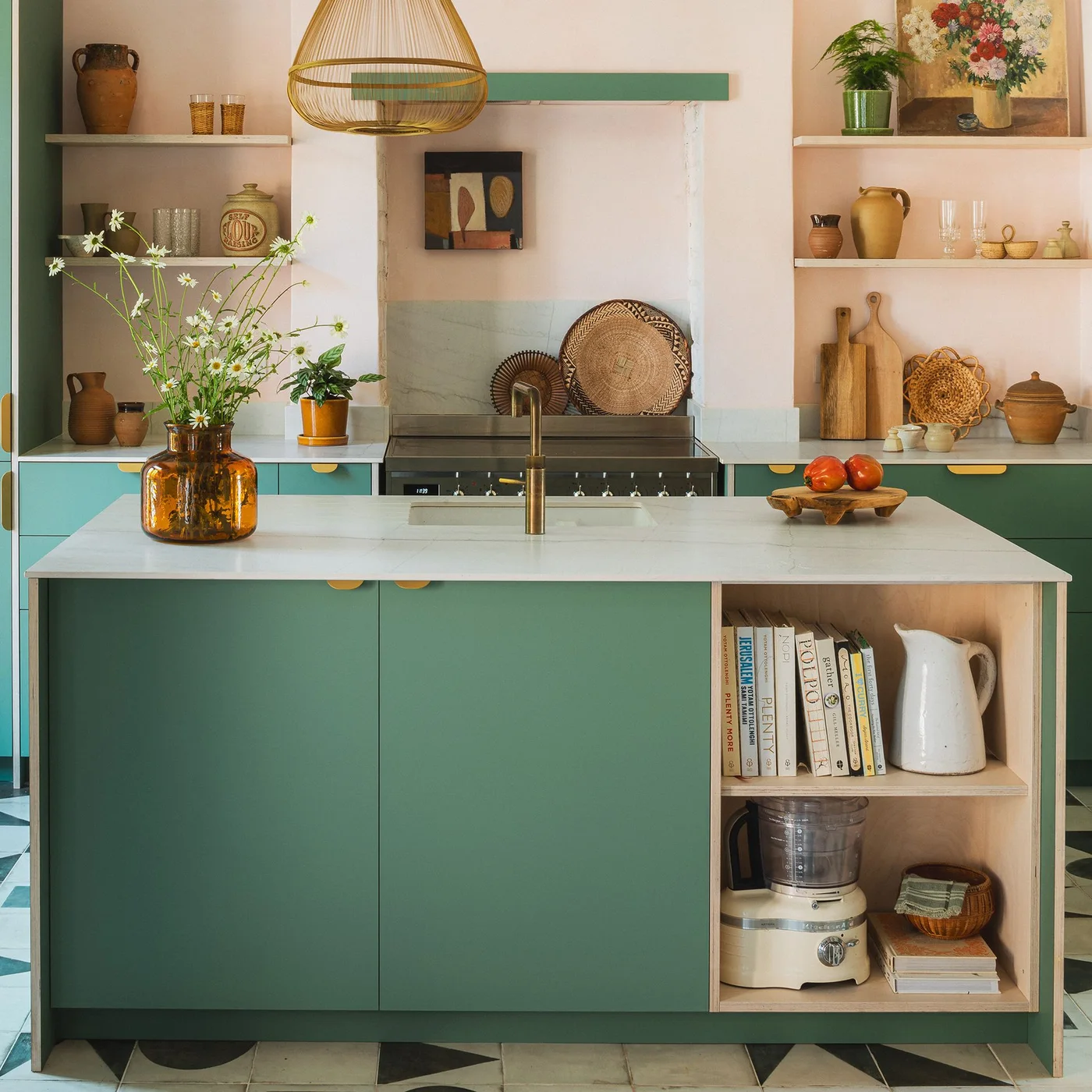 Green cabinet fronts with warm semicircular pulls sit beside open wooden island shelves beneath pale counters and warmer walls