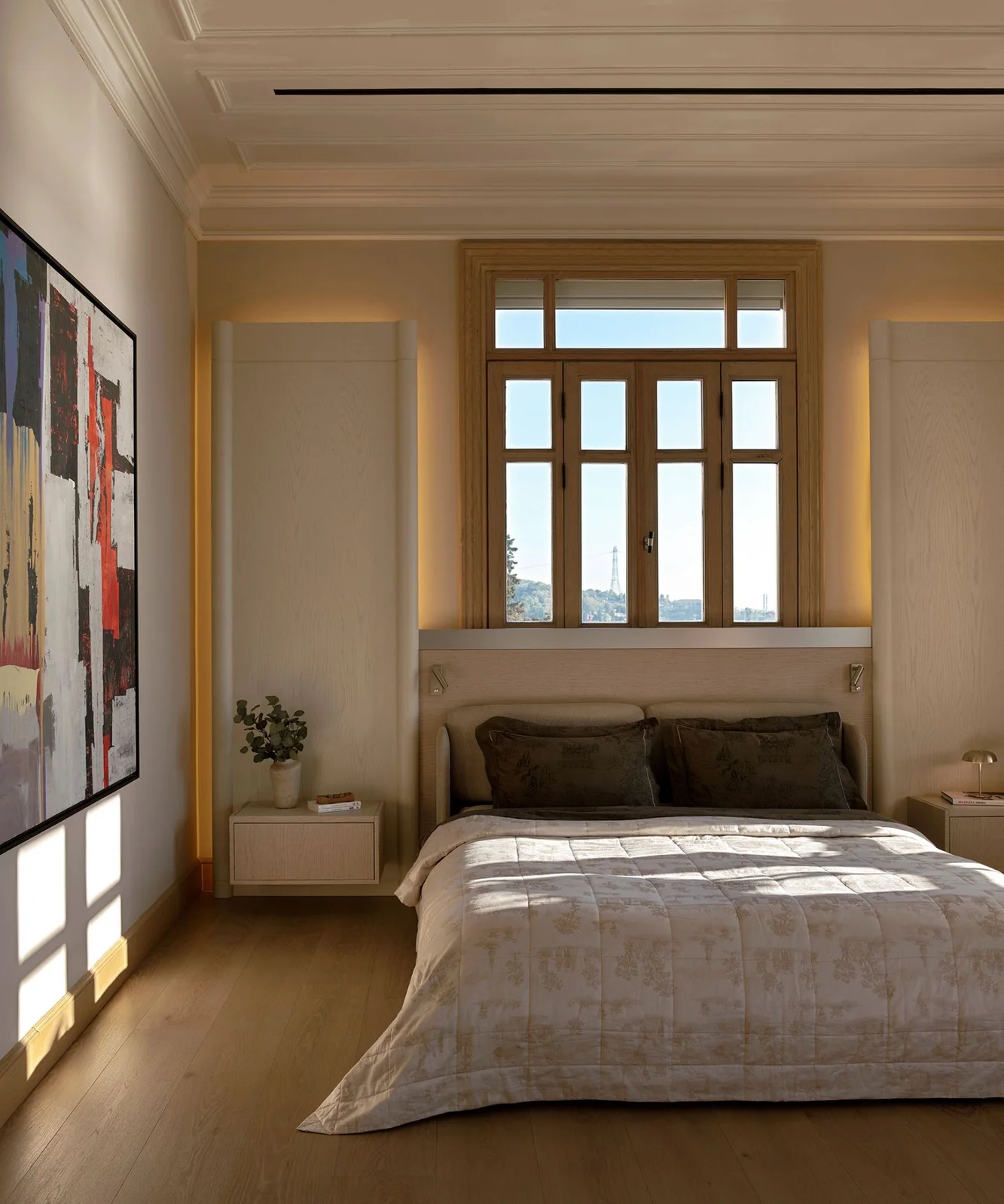 A pale bed sits beneath a tall window between wall panels with warm edge lighting and two small floating bedside cabinets