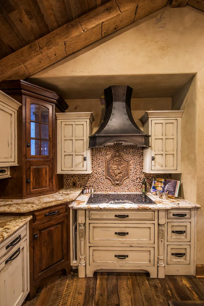Cream cabinets sit below a dark hood in a kitchen with exposed beams and warm wood storage