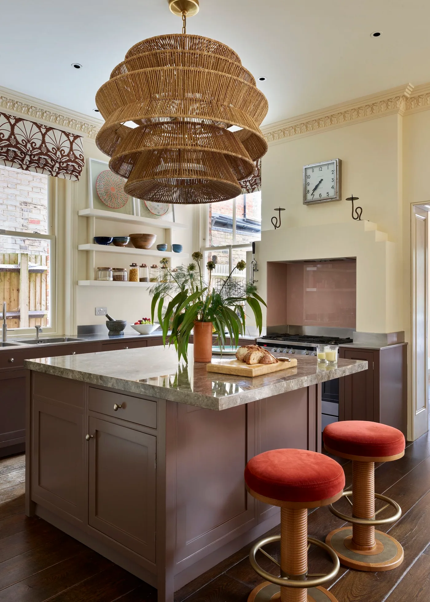 Brown painted kitchen island and lower cabinets with a large woven pendant and two rust-red stools.