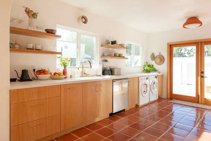 Honey-toned timber base cabinets, floating timber shelves and terracotta floor tiles in a real kitchen