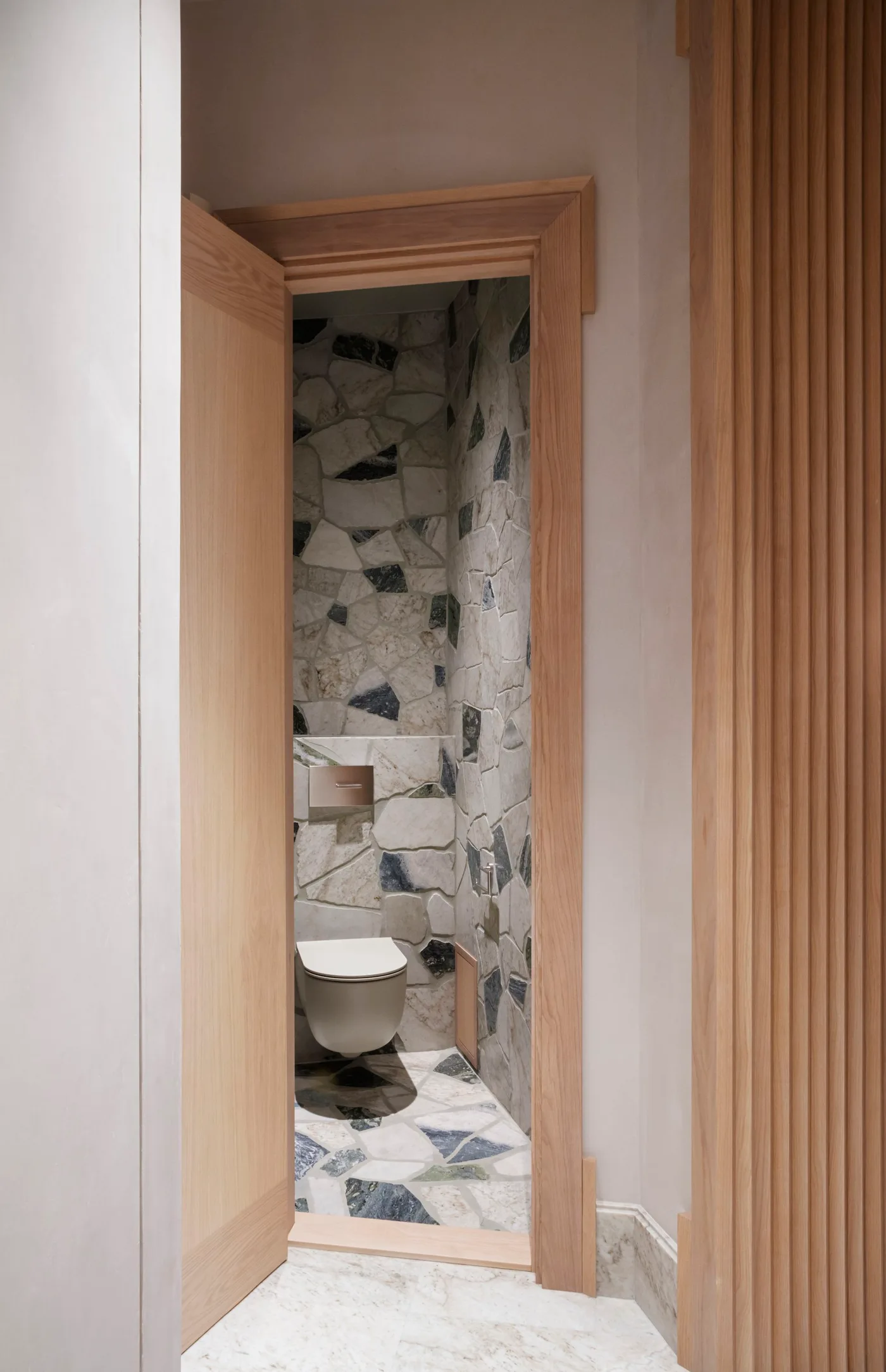 Irregular pale and dark mineral-pattern wall and floor surfaces inside a wood-trimmed bathroom doorway