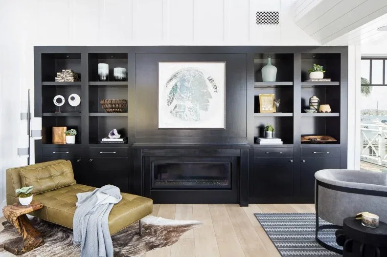 Living room with dark built-in fireplace wall, open display shelves, closed lower cupboards, green low chair, wooden side table and gray curved seating.