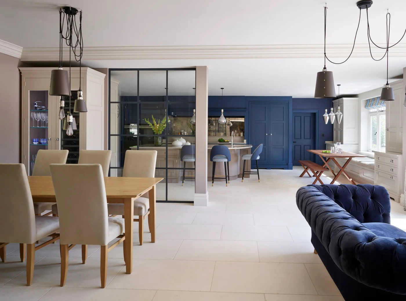 A black-framed partial screen separates a pale dining area from a blue kitchen beside a blue sofa