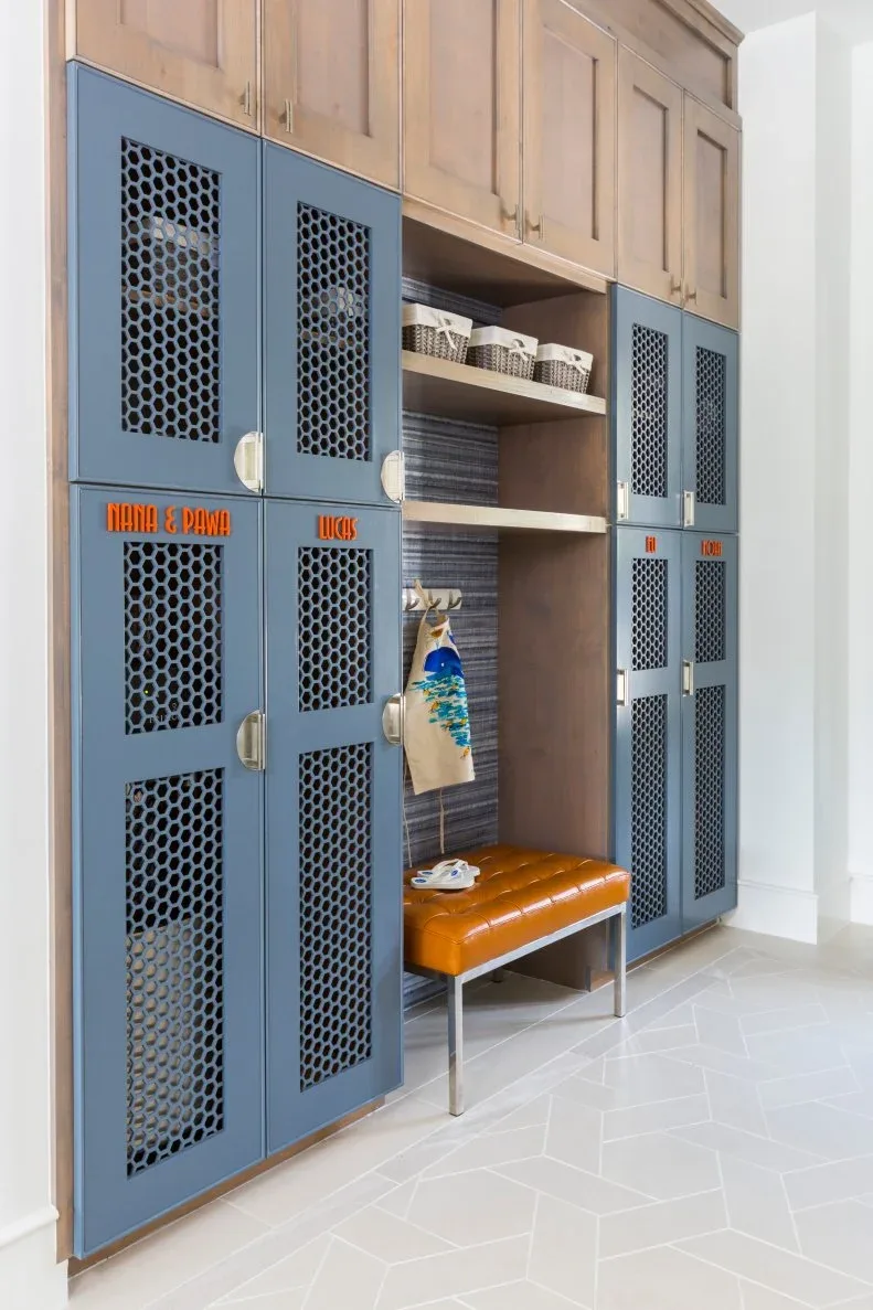 Entry storage with blue mesh-front cupboard doors, wood upper cupboards, central small orange bench and open shelves