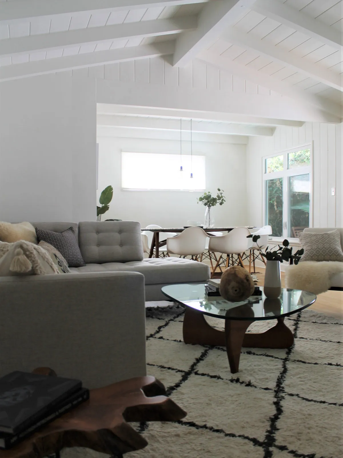 Pale painted beams span a bright living room above gray seating and a lightly patterned rug.