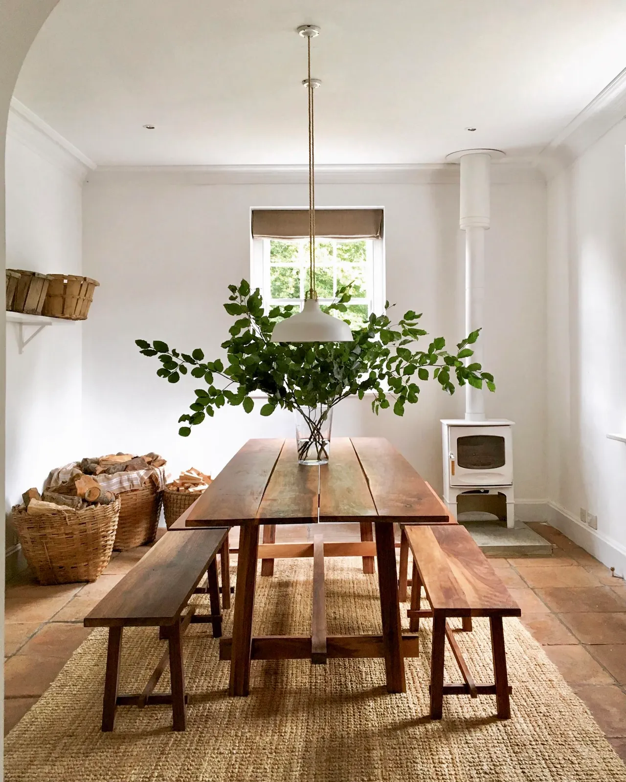 A timber table and benches sit in a pale room beneath a simple pendant.