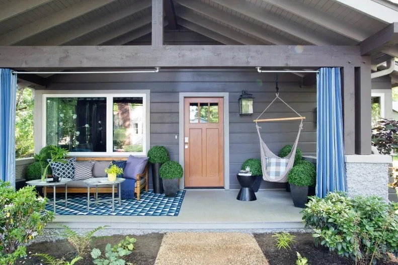 Gray cottage porch with wood sofa, suspended hammock chair, blue curtains and patterned blue rug