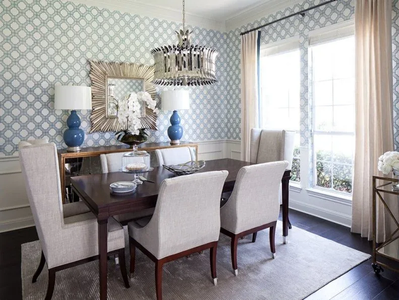 Blue-and-white patterned dining room with pale high-backed chairs, a dark table, paired blue lamps and a broad framed mirror